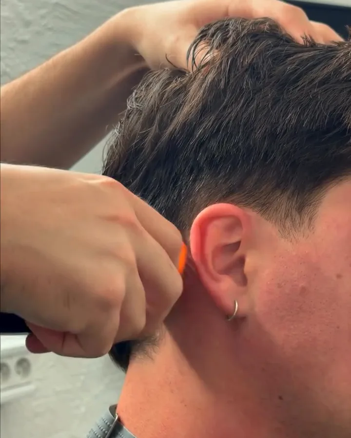 La main gauche du barbier posée sur la tête du client, la tondeuse et son sabot orange à la nuque